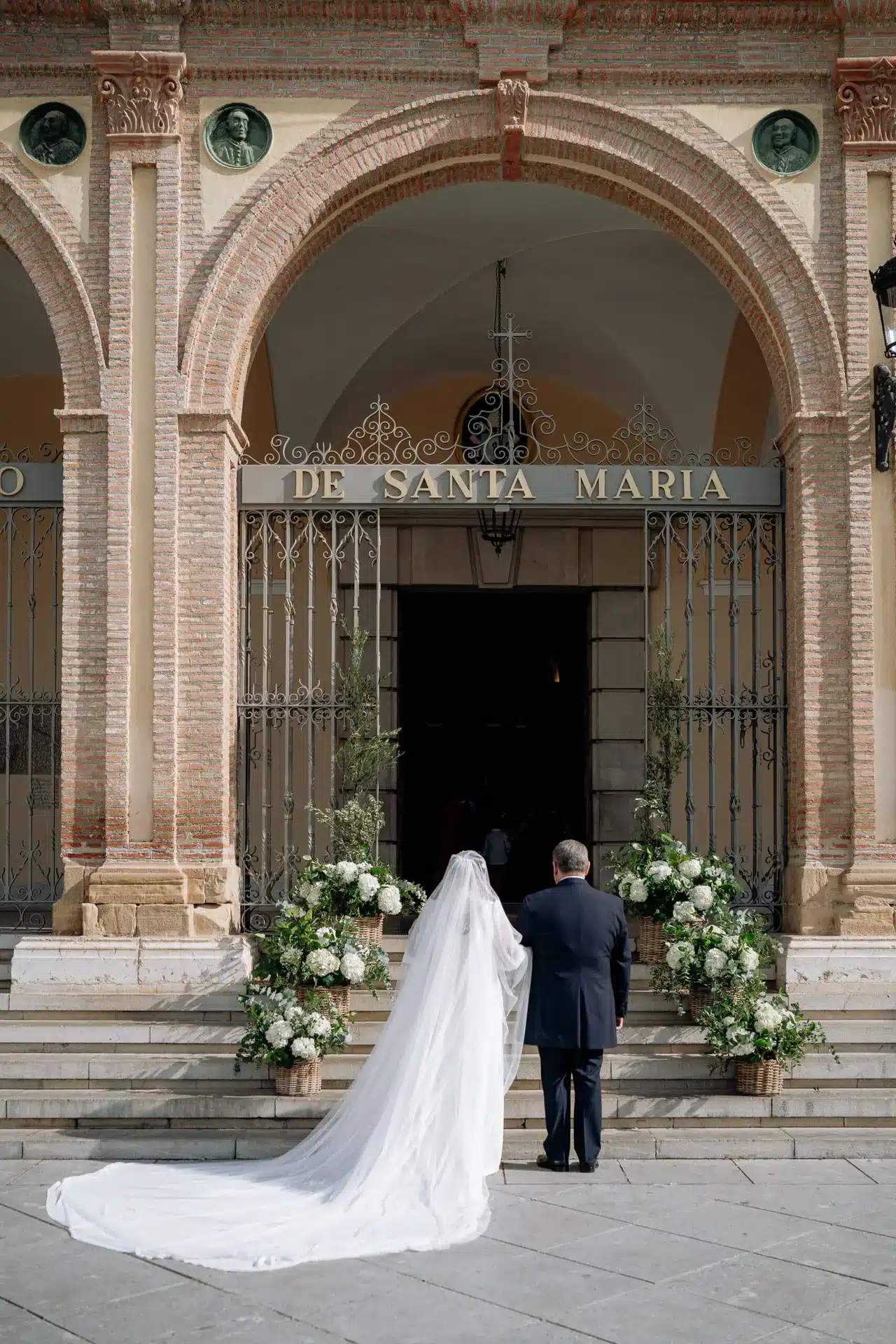Entrada de ceremonia novia y padrino. Iglesia Santuario de la Victoria, Málaga. Iglesia decorada con cestas y flores blancas