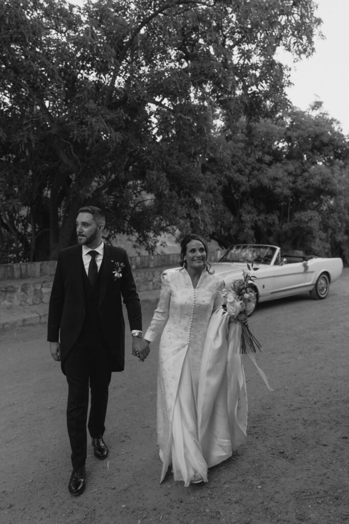 Elizabeth y Louis paseando junto a un Mustang blanco el día de su boda en Coín, Málaga