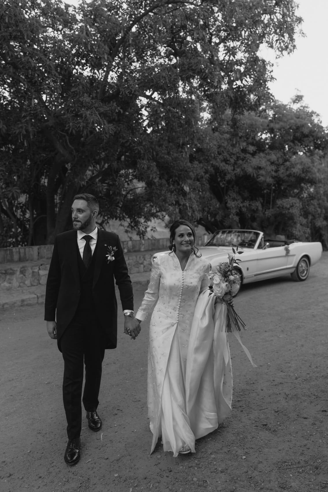 Elizabeth y Louis paseando junto a un Mustang blanco el día de su boda en Coín, Málaga